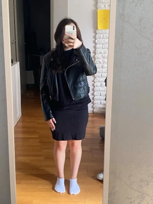 Svart biker skinnjacka med dragkedjor - Snygg svart skinnjacka i bikerstil med silvriga dragkedjor och fickor. Kort modell som sitter och har klassiska detaljer som bred krage och axelparti. Perfekt för en cool och trendig look. Har blivit konstigt böjd vid kragen, se sista bilderna. Egentligen storlek M, men passar som XS bättre. Har katter hemma!!!