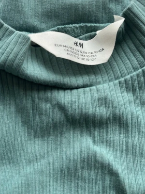 Ribbad grön stickad tröja H&M - Snygg ribbad stickad tröja i en mjuk grön färg från H&M. Tröjan har långa ärmar och en enkel, rund halsringning. Perfekt för dig som gillar en stilren och bekväm look. Materialet är stretchigt och följsamt.