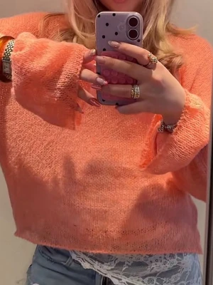 Persikofärgad stickad tröja - Trendig stickad tröja i persikofärg med lös passform och vida ärmar. Tunt och luftigt material som ger en avslappnad look. Perfekt att styla med jeans eller kjol för en cool vardagsstil.