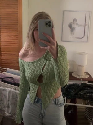 Grön off shoulder topp med struktur - Trendig ljusgrön långärmad topp med off shoulder-modell och vågig struktur. Toppen har asymmetrisk nederkant och cut-out-detaljer framtill. Perfekt för dig som vill sticka ut med en unik och modern stil. Från SHEIN i storlek S. Aldrig använd.