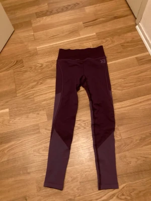 Mörklila träningstights från Better Bodies  - Snygga mörklila träningstights från Better Bodies med hög midja och kontrasterande paneler längs benen. Tillverkade i stretchigt funktionsmaterial som passar perfekt för gymmet eller löprundan. Diskret logga på höften och tight passform.Nya!!!