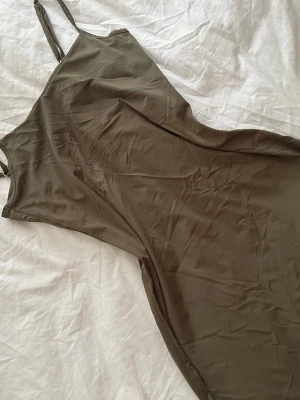 Olivgrön ärmlös klänning - En stilren olivgrön klänning med smala axelband och slät design. Klänningen har en enkel och elegant form som passar perfekt för dig som gillar minimalistiska plagg. Materialet känns mjukt och lätt, vilket gör den bekväm att bära.