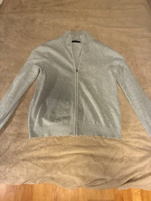 Ljusgrå ziptröja från Selected Homme - Ljusgrå ziptröja från Selected Homme med hög krage och ribbade muddar. Tröjan har hel dragkedja framtill och är tillverkad i mjukt material, perfekt för lager på lager. Enkel och stilren design som passar till det mesta.