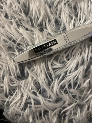 L'Oréal False Lash Mascara silver - Snygg mascara från L'Oréal i modellen False Lash. Höljet är i blankt silverfärgat plastmaterial med svart och vit text. Perfekt för att ge fransarna extra volym och längd. Modern och stilren design som känns lyxig i sminkväskan.