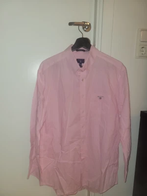 Ljusrosa skjorta från Gant - Klassisk ljusrosa skjorta från Gant med button-down krage och broderad logga på bröstfickan. Skjortan har långa ärmar, normal passform och är tillverkad i mjuk bomull. Perfekt för en clean och stilren look.