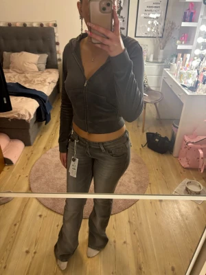 Grå bootcut jeans från Gina tricot  - Säljer ett par grå bootcut jeans från Gina tricot med låg midja och snygga detaljer på bakfickorna. Jeansen har klassisk femficksdesign och är tillverkade i stretchigt denimtyg för en bekväm passform. Perfekta för en trendig och avslappnad look.