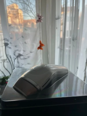 Vit IPL hårborttagningsapparat - Säljer en vit IPL hårborttagningsapparat med ergonomisk form och slimmad design. Perfekt för smidig hårborttagning hemma. Apparaten har en stor knapp på ovansidan och är tillverkad i plast.