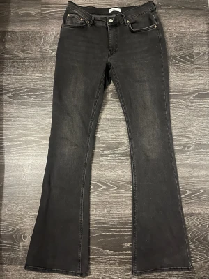 Svarta bootcut jeans strl 42 - Säljer ett par svarta ish mörkgrå bootcut jeans med  utsvängda ben och klassisk femficksmodell. Jeansen har en snygg tvättad look och är tillverkade i stretchigt material för extra komfort. Strl 42. Endast använd 2 ggr!!