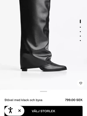 Svarta höga stövlar med klack - Säljer ett par svarta höga stövlar med låg klack och slouchy passform. Stövlarna har spetsig tå och är tillverkade i ett glansigt skinnliknande material. De har en unik design där skaftet liknar byxben och täcker hela vaden.