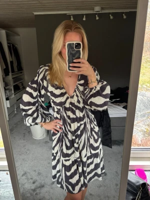 Svartvit  klänning -  kort klänning med svartvitt zebramönster och v-ringning. Klänningen har långa puffärmar och en lös passform 