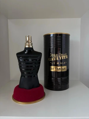 Jean Paul Gaultier Le Male Le Parfum - Maskulin parfymflaska från Jean Paul Gaultier i form av en svart torso med gulddetaljer. Flaskan står på en rund röd sammetsliknande bas och kommer med en svart och guld cylinderformad förpackning. Perfekt för dig som gillar exklusiva och ikoniska dofter. Ungefär 60ml kvar.