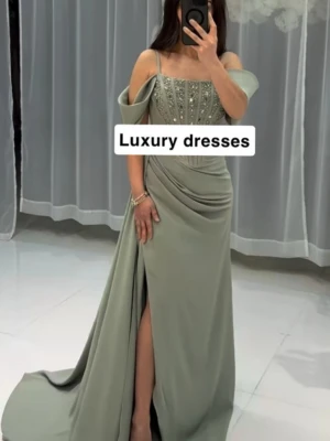 Klänning bal/fest - Elegant ljusgrön långklänning med offshoulder och tunna axelband. Livet är dekorerat med pärlor och har en snygg drapering över höften. Klänningen har en slits framtill och ett svepande fall. Perfekt för bal, fest eller student. 