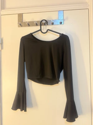 Svart croppad topp med trumpetärmar - 2st  - En svart, croppad topp med långa ärmar och snygga trumpetärmar. Toppen har en enkel, rund halsringning och är tillverkad i ett mjukt och stretchigt material. Perfekt för dig som gillar en trendig och stilren look. 2 tröjor båda för 100kr 