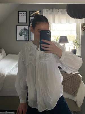 Vit blus från Zara - Snygg vit blus från Zara med volangdetaljer och rynkade partier framtill. Blusen har en avslappnad passform, knäppning framtill och långa ärmar med lätt puff. Perfekt att styla med jeans för en trendig look.