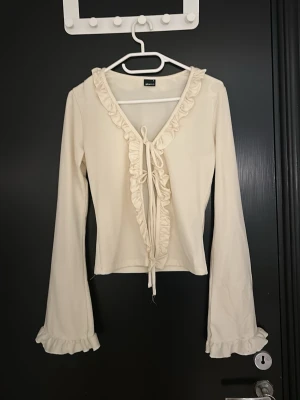 Beige volangtop med knyt från Gina Tricot - Supersöt beige topp från Gina Tricot med volangkant längs v-ringningen och knyt framtill. Tycker denna tröjan är jättefin men säljer för att den inte används så mycket. Perfekt till våren!