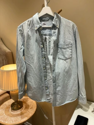 Ljusblå skjorta från Zara - Säljer en stilren ljusblå skjorta från Zara med klassisk krage och bröstficka. Skjortan har knappar framtill och långa ärmar. Perfekt för en avslappnad men snygg look.