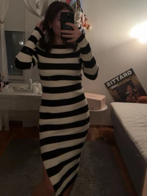 Svartvit randig långklänning - Snygg långärmad långklänning med breda svarta och vita ränder. Klänningen har en kroppsnära passform och rund halsringning. Perfekt för dig som gillar en stilren och trendig look. Från reserved och aldrig använd. 