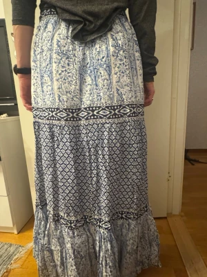 Långkjol - Säljer en jättefin långkjol i blått och vitt med mixade mönster perfekt till utomlandsresorna och sommaren.  Kjolen har volangkant nertill och är tillverkad i ett lätt, flowy material som passar perfekt till vår och sommar. Pris diskuterbart vid snabb affär 💕 