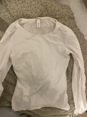 Vit långärmad topp från H&M - En enkel och stilren vit långärmad topp från H&M. Toppen har rund halsringning och är gjord i mjuk bomull, perfekt att matcha med jeans eller kjol. Passformen är normal och materialet känns bekvämt mot huden.