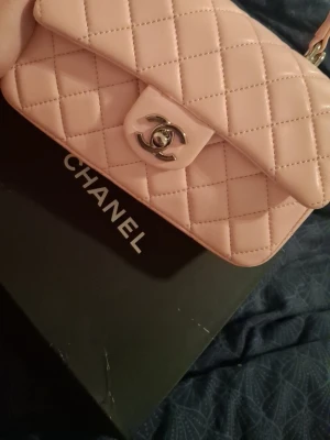 Ljusrosa  handväska - Supersnygg ljusrosa handväska med klassiskt silverfärgat . Väskan har en stilren, rektangulär form och ett elegant handtag upptill. Perfekt för dig som vill ha en ikonisk accessoar med lyxig känsla.