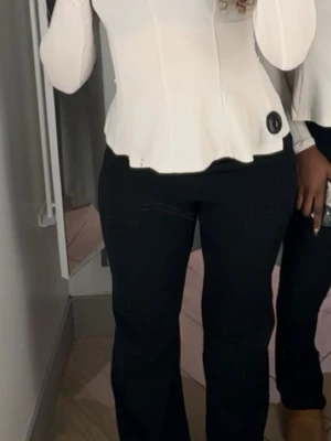 Vit figurnära korsettopp - Snygg vit korsettopp med figurnära passform och lätt utsvängd nederkant. Toppen har långa ärmar och markerad midja som ger en feminin siluett. Perfekt att styla med jeans eller kjol för en trendig look.