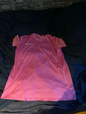 Rosa tränings-tshirt från Craft - Säljer en rosa tränings-tshirt från Craft i funktionsmaterial. T-shirten har rund halsringning och korta ärmar, perfekt för träning eller sportaktiviteter. Logga på bröstet och lätt, snabbtorkande tyg.