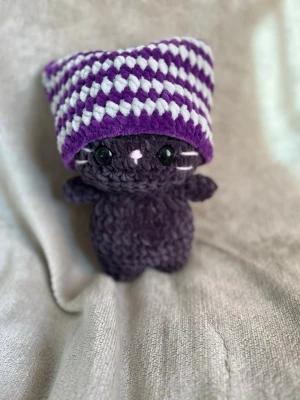 Virkad katt med lila-vit mössa - Katten är ca 24 cm hög och har en avtagbar mössa 🌸 katten har Säkerhetsögon som inte rekommenderas för barn under tre år!