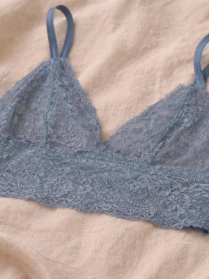 Blå spetsbralette med smala band - Säljer en blå bralette i mjuk spets med blommigt mönster och smala axelband. Modellen har triangelformade kupor och bred spetskant nedtill för extra komfort. Perfekt för dig som gillar en enkel och stilren look.