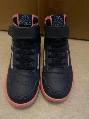 Marinblå Kappa sneakers med rosa detaljer - Snygga marinblå sneakers från Kappa med rosa sula och foder. Skorna har svarta skosnören, kardborreband upptill och ventilerande meshdetaljer. Perfekt för dig som gillar sportig stil och vill sticka ut med färgade detaljer.