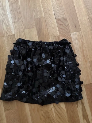 Svart paljettkjol i polyester XS/s - Säljer en svart kortkjol med stora paljetter som ger ett riktigt coolt och glittrigt uttryck. Kjolen är tillverkad i 100% polyester. Aldrig använd bara provad, inga defekter. Lite större i storleken så skulle säga stt den passar xs/s💕💕