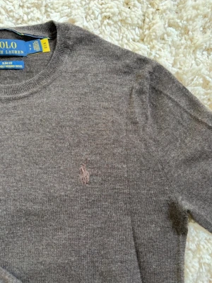 Stickad tröja Polo Ralph Lauren - Mjuk och stilren brun stickad tröja från Polo Ralph Lauren i merinoull. Tröjan har rund halsringning, långa ärmar och diskret broderad logga på bröstet. Slim fit-modell som passar perfekt till jeans eller chinos. 