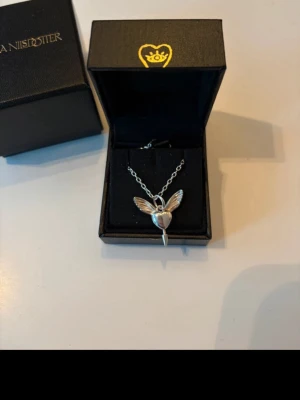 Silverhalsband Maria Nilsdotter - Unikt halsband i silver från Maria Nilsdotter med ett hängsmycke format som en hjärtformad figur med vingar. Kedjan är tunn och smycket har en modern, stilren design. Perfekt för dig som gillar detaljerade och personliga accessoarer.