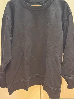 Svart sweatshirt från GANT - Klassisk svart sweatshirt från GANT med diskret broderad logga på bröstet. Tröjan har rund halsringning, långa ärmar och ribbade muddar vid ärmslut och nederkant. Perfekt basplagg i mjukt bomullsmaterial.