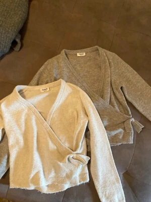 Två omlottkoftor från Kappahl - Säljer två mjuka omlottkoftor från Kappahl, en i ljusbeige och en i grått. Båda har långa ärmar, ribbade muddar och knytband i midjan. Perfekta för lager på lager och riktigt sköna att ha på sig.