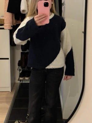 Mörkblå och vit stickad tröja - Säljer en stickad tröja i mörkblått och vitt med coolt, asymmetriskt färgblocksmönster. Tröjan har rund halsringning och långa ärmar. Perfekt för dig som gillar en avslappnad men trendig stil.
