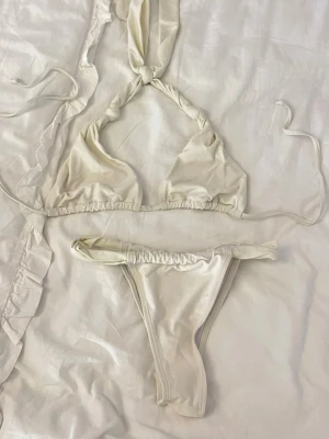 Vit bikini med knyt och twist - Trendig vit bikini med twistade detaljer och knyt i nacken. Triangeltopp och matchande bikinitrosa med smala band i sidorna. Perfekt för stranden eller poolen. Materialet känns mjukt och följsamt.