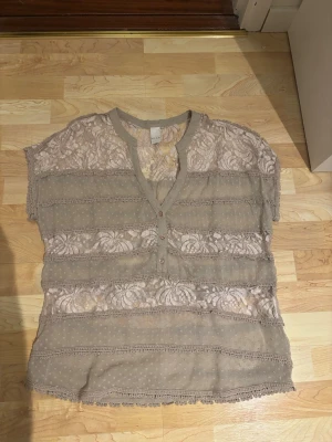 Beige blus med knappar och spets - En beige blus som är genomskinlig med spets både framtill och baktill. Perfekt att ha till jeans med ett linne under. Är väldigt oversized.