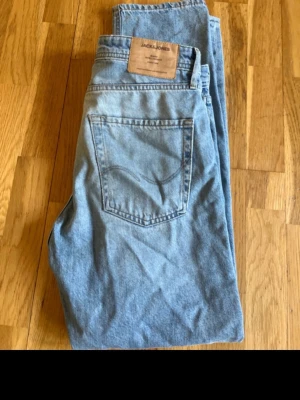 Ljusblå jeans från Jack & Jones - Snygga ljusblå jeans från Jack & Jones i klassisk rak modell. Jeansen har fyra fickor och en läderpatch med logga bak i midjan. Tillverkade i bomull med en mjuk denimkänsla. Perfekta för en avslappnad och trendig stil.