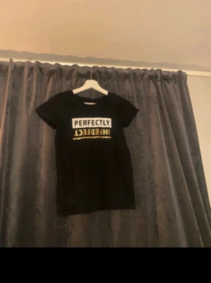 Svart t-shirt med tryck - Cool svart t-shirt från New Look med texten 'PERFECTLY IMPERFECT' i vitt och gult på bröstet. T-shirten har en klassisk rund hals och korta ärmar, perfekt för en avslappnad och trendig look.