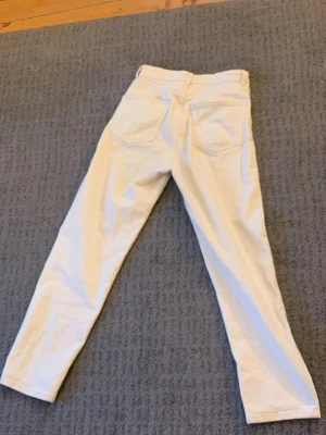 Vita raka jeans med hög midja - Säljer ett par vita jeans med raka ben och hög midja. Jeansen har klassiska bakfickor och är i ett stilrent, tidlöst snitt. Perfekta att matcha med sneakers eller boots för en clean look.