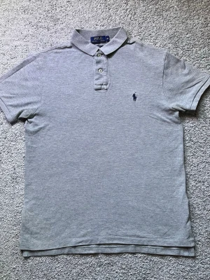 Grå pikétröja Polo Ralph Lauren - Tjena, säljer denna gråa piké från Ralph lauren. Tröjan är storlek M, i princip aldrig använd. Tröjan är 66cm lång, 44cm axelbred. Skriv om du undrar något så löser vi det! (PRISET ÄR INTE FAST)