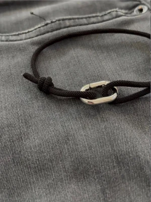 Svart armband  - Stilrent svart armband i justerbar textilsnodd med ett minimalistiskt silverfärgat metallspänne. Perfekt accessoar för en enkel men cool look. Passar både tjejer och killar och är lätt att matcha med andra smycken.