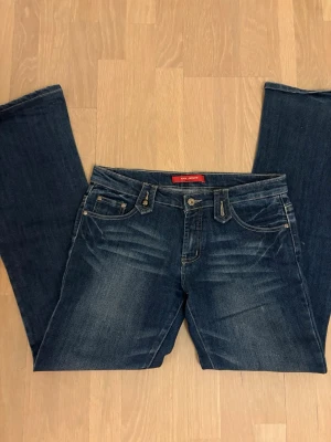 Blå bootcut jeans från XFN Jeans - Säljer ett par blå bootcut jeans från XFN Jeans med snygga slitningar och kontrastsömmar. Klassisk femficksmodell och normalhög midja. Perfekta för dig som gillar en avslappnad men trendig look.
