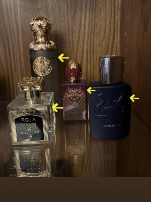 Fyra exklusiva parfymer mixade märken - Samling av fyra lyxiga parfymer: en genomskinlig flaska med guldlock från Roja, en svart flaska med silverdetaljer från Parfums de Marly, en lila flaska med gulddetaljer och röd kork från Clive Christian samt en svart flaska med gulddetaljer från Xerjoff. Alla flaskor har unika, eleganta designer.