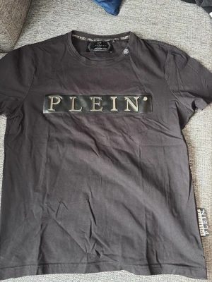 Svart t-shirt från Philipp Plein - Säljer en svart t-shirt från Philipp Plein med stort PLEIN-tryck i silver på bröstet.  det står strl L men skulle säga den passar S
