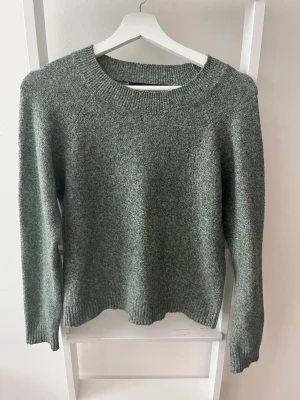 Grön stickad tröja från Vero Moda - Mysig grönmelerad stickad tröja från Vero Moda med rund halsringning och långa ärmar. Tröjan har ribbade muddar vid hals, ärmslut och nederkant. Enkel att matcha med jeans eller kjol. Köparen står för eventuell frakt.