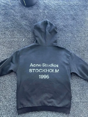 Svart hoodie Acne Studios Stockholm - Riktigt snygg och fräsch hoodie från Acne Studios. Allt är i fint skick men texten lossnar såklart långsamt efter tid. (Skriv vid funderingar)
