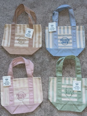 Randig mini shoppingväska Trader Joe's - Säljer en randig minishoppingväska från Trader Joe's i canvas. Finns i flera färger: beige, blå och grön. Väskan har breda axelband, broderad logga på framsidan och praktisk ficka. Perfekt för att bära småsaker eller som accessoar. Denna annons står för den blåa väskan.💗