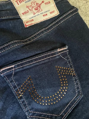 True religion Bootcut jeans - Intressekoll på dessa unika mörkblå bootcut jeans från True Religion med kontrastsömmar och gulddetaljer på bakfickorna. De är i stretchigt material och passar mig som annars har w25/w26. Klassisk femficksmodell och mjukt denimtyg. Perfekta för dig som vill ha en cool och unik look. Pris är diskuterbart