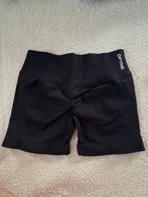 Svarta träningstights från DFYNE - Säljer ett par svarta träningstights från DFYNE med hög midja och ribbad linning. Shortsen har en tight passform och scrunch-detalj bak för extra form. Perfekta för gymmet eller andra träningspass.
